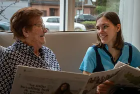 Résidente et membre de l'équipe paramédicale lisant un journal à la résidence Ter Eyke