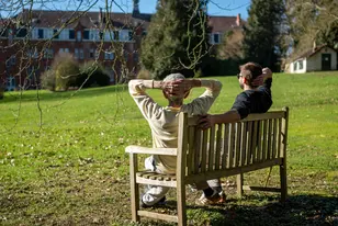 Résident et kiné assis sur un banc et profitant du soleil à la résidence Chateau Chenois