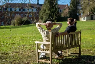 Résident et kiné assis sur un banc et profitant du soleil à la résidence Chateau Chenois