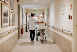 Résidente et infirmière marchant dans un couloir à la résidence De Bottelarij