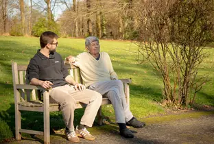 Résident et kiné assis sur un banc et profitant du soleil à la résidence Chateau Chenois