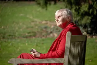 Résidente profitant du soleil assise sur un banc à la résidence Château Chenois dans le cadre du projet Living