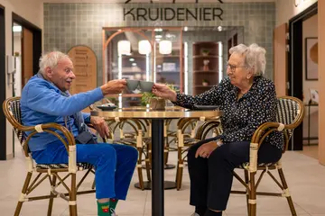 Deux résidents trinquant avec un café à une table du salon/bar de la résidence Boschart