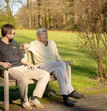 Résident et kiné assis sur un banc et profitant du soleil à la résidence Chateau Chenois