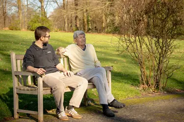 Résident et kiné assis sur un banc et profitant du soleil à la résidence Chateau Chenois