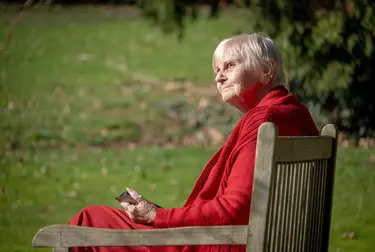 Résidente profitant du soleil assise sur un banc à la résidence Château Chenois dans le cadre du projet Living