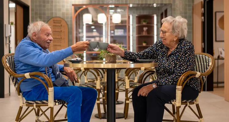Deux résidents trinquant avec un café à une table du salon/bar de la résidence Boschart